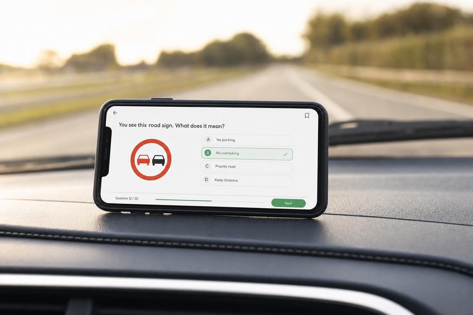 Smartphone mit einer Lern-App-Oberfläche auf dem Armaturenbrett eines Fahrschulautos, im Hintergrund unscharf die Straße durch die Windschutzscheibe